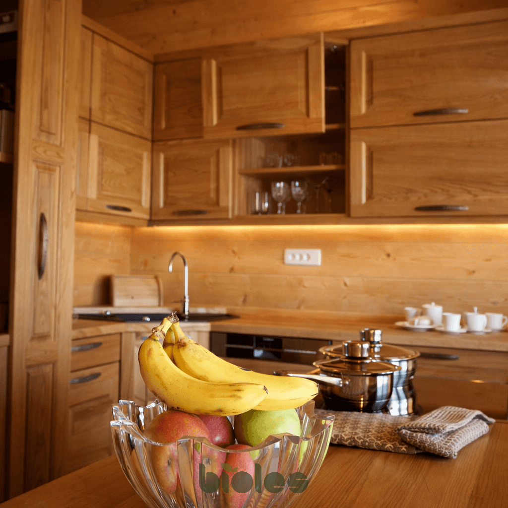 Schüssel mit Bananen und Äpfeln auf einem Holztisch in einer modernen Küche.