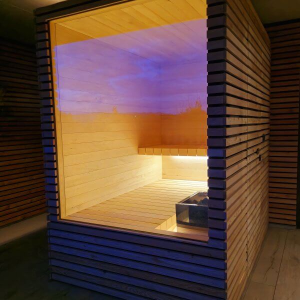 Moderne Sauna aus Holz mit beleuchtetem Innenraum und Glasfront.